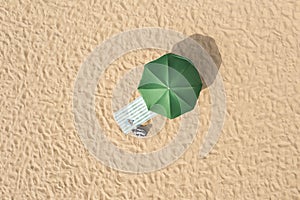 Beach umbrella near towel and other vacationist`s stuff on sand, aerial view