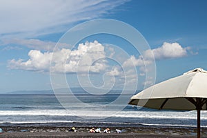 Beach umbrella on a sunny day, sea in background. Tropical beach with black sand. Beautiful sky. Paradise island Bali