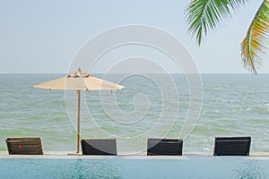 Beach umbrella and wooden chair nearly swimming pool.