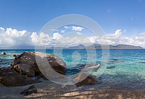 The beach is on uninhabited and wild subtropical island. Beautiful sea, clear sky, mountains in the distance. Large stones