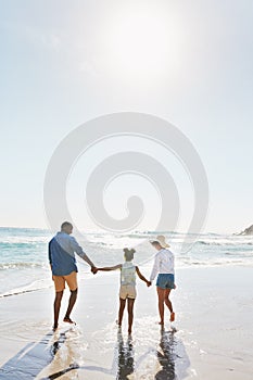 Beach vacation and couple with child walking in water while holding hands together with love in summer from the back