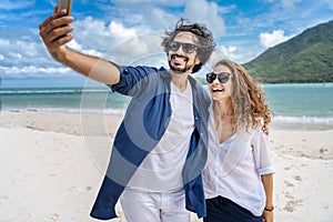 Beach vacation couple taking selfie photograph using smartphone relaxing and having fun holding smart phone camera. Young