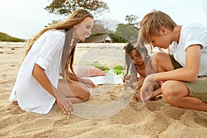 Beach Vacation. Family Enjoying Summertime At Tropical Resort. Mother And Little Girl Burying Boy In Sand.