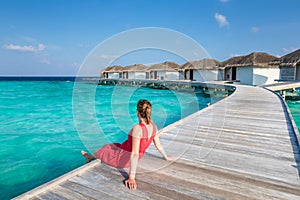 Beach vacation holidays with woman relaxing on wooden pier at luxurious hotel resort in Maldives with overwater villas, turquoise