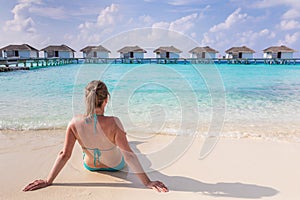 Beach vacation holidays with woman sun bathing on white sand at luxurious hotel resort in Maldives with overwater villas,