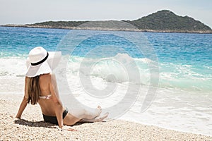 Beach vacation. Hot beautiful woman in sun hat and bikini standing with her arms raised to her head enjoying looking view of beach