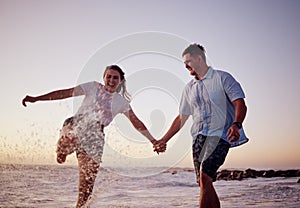 Beach water splash, couple and happy people together feeling love and fun in summer at sunset. Girlfriend and boyfriend