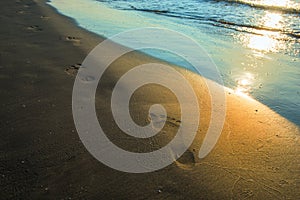 Beach wave and footprints at sunset time