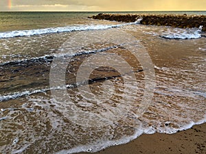 Beach with waves and foam and skyline with rainbow