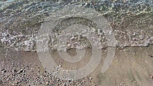 Beach waves, sand and pebble seabed under clear water of the sea. Coastal nature concept