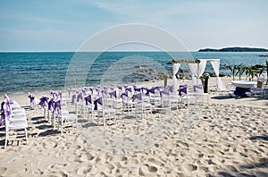 Beach wedding venue setup seaside with white chiavari chairs with purple organza sash decoration