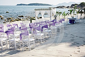 Beach wedding venue settings with white chiavari chairs decorate with violet organza sash at seaside