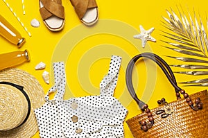 Beach wicker straw or rattan women`s eco bag, white dress straw hat sandals golden tropical leaf on yellow background Flat lay to