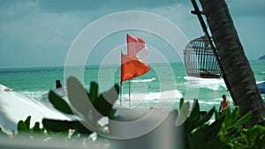 Beach wind warning red flag stuck in the sand with waves crashing on the shore