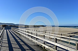 Beach with wooden boardwalk, dunes and wild sea with waves. Blue sky, Galicia, Spain.