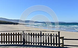 Beach with wooden boardwalk and handrail. Wild sea with waves and blue sky. Arteixo, Coruna, Galicia, Spain.