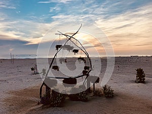 A beach with a wooden triangle frame hanging some flowers