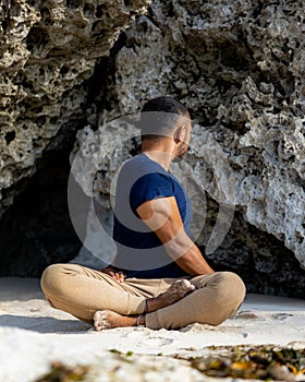 Beach yoga. Asian man practicing Parivrtta Sukhasana outdoor. Sitting in variation of Lotus pose. Easy twist pose. Stretching hips