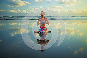 Beach yoga. Attractive woman practicing Gomukhasana. Cow Face Pose. Hands in namaste mudra. Closed eyes. Water reflection. Zen