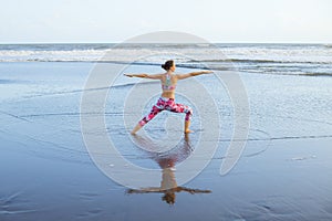 Beach yoga. Caucasian woman practicing Virabhadrasana II, Warrior II Pose. Strong body. Healthy lifestyle. Water reflection. Yoga