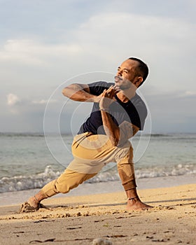 Beach yoga practice. Parivrtta Anjaneyasana, Twisted High Lunge Pose. Hands in namaste mudra. Asian man practicing yoga on the