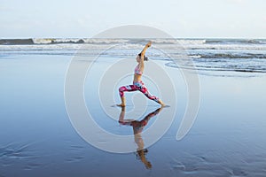 Beach yoga. Slim Caucasian woman practicing Virabhadrasana II, Warrior II Pose. Strong body. Healthy lifestyle. Water reflection.