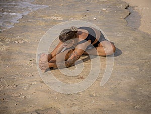 Beach yoga. Woman practicing Janu Shirasasana or Head-to-Knee Pose. One-Legged Forward Bend. Seated twisting and forward bending