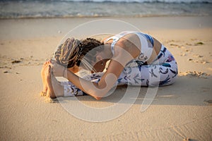 Beach yoga. Young woman practicing Paschimottanasana, Seated Forward Bend Pose. Flexible body. Stretching exercise. Healthy spine