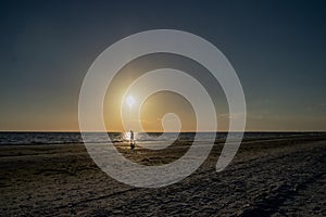 Beachcomber walks Fort Myers Beach during sunset with sailboat i