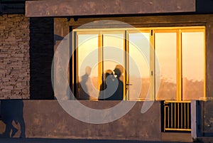 Beachgoers reflections at windows of a  beach house brightly lid by sunset