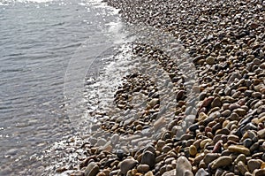 Beachline covered by colorful pebbles washed by waves