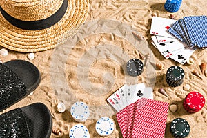 Beachpoker. Chips and cards on the sand. Around the seashells, hat and flip flops. Top view