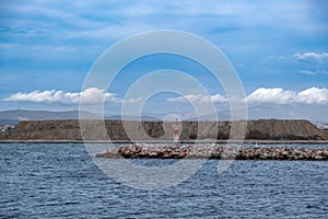 Beacon lighthouse on breakwater rocky wall construction at harbor entry of Greek island background