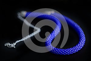 Bead crochet necklace blue color a dark surfce close up. Fashion background