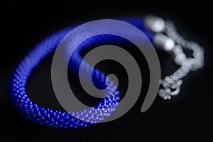 Bead crochet necklace blue color a dark surfce close up. Fashion background