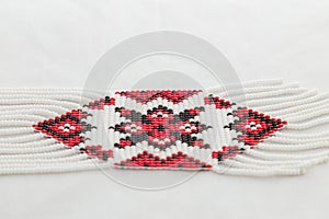Beaded ethnic red and black necklace on white fabric background. Female accessories, decorative ornaments and jewelry. Fashion