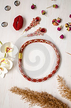 Beaded necklace and brooch set. Red garnet soutache jewelry on the white wooden background. Women accessories