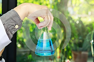 Beaker with blue experiment liquid in scientist hand on laboratory background, science concept