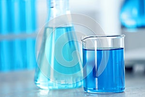Beaker with light blue on table in laboratory. Space for text