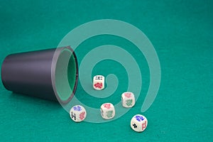 A beaker with poker dice on a green table