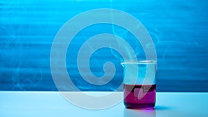 Beaker with smoke on a table of a chemical laboratory. Blue background.