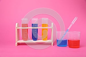 Beakers and test tubes with colorful liquids in wooden stand on bright pink background. Kids chemical experiment set