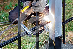 A beam of bright sparks from electric arc welding flies in different directions on a blurred background of the welder and green