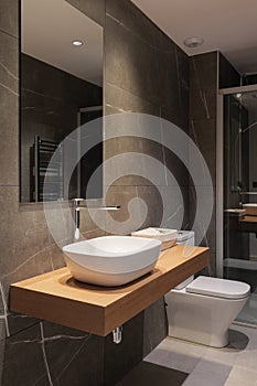 Beam from lamp illuminates white deep sink on marble countertop in noble wood color. Large mirror on wall reflects