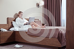 Beaming appealing woman working on laptop while lying in bed