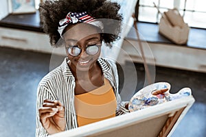 Beaming artist with nice makeup smiling while painting