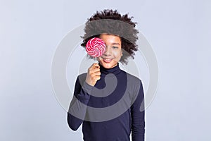 Beaming curly young guy closing his face with sweet red candy