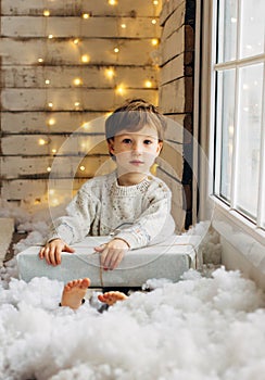 Beaming curlyhair boy opening his christmas gift. New Year lights background