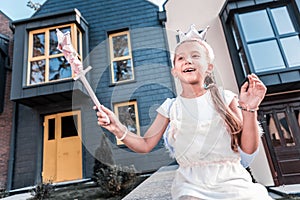 Beaming dark-haired girl with magic wand walking near her house