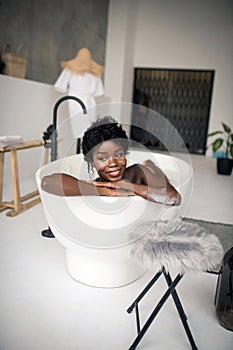 Beaming dark-skinned woman having rest in bath at the weekend